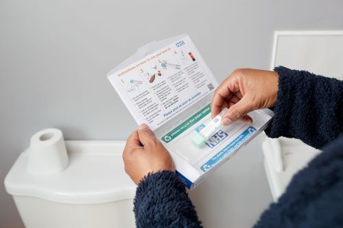 Photo showing a man in a bathroom opening a bowel cancer screening test kit from NHS England